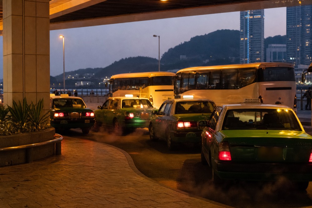 A taxi rank and resort shuttle bay outside a Macau ferry terminal at dusk