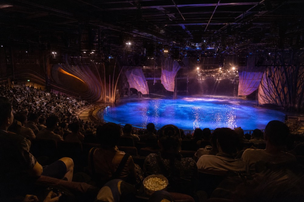 Wide view over a tiered aquatic theatre audience toward a lit stage