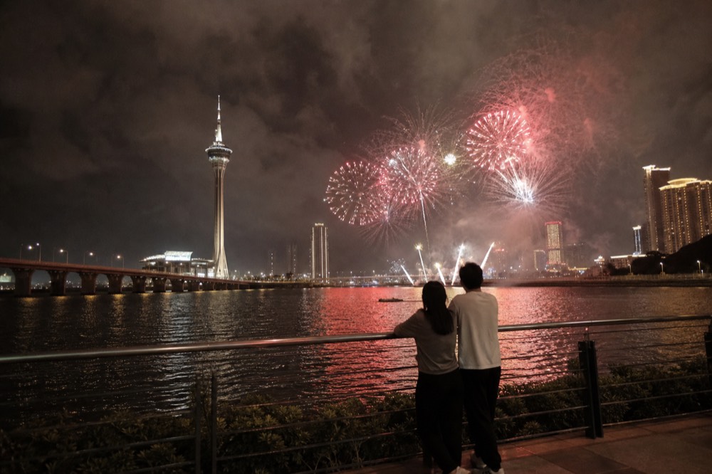 Fireworks bursting over a night harbour with a tower silhouette