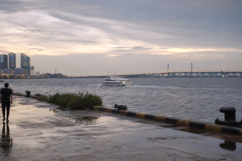 A hydrofoil ferry and a road bridge seen across a harbour at dusk