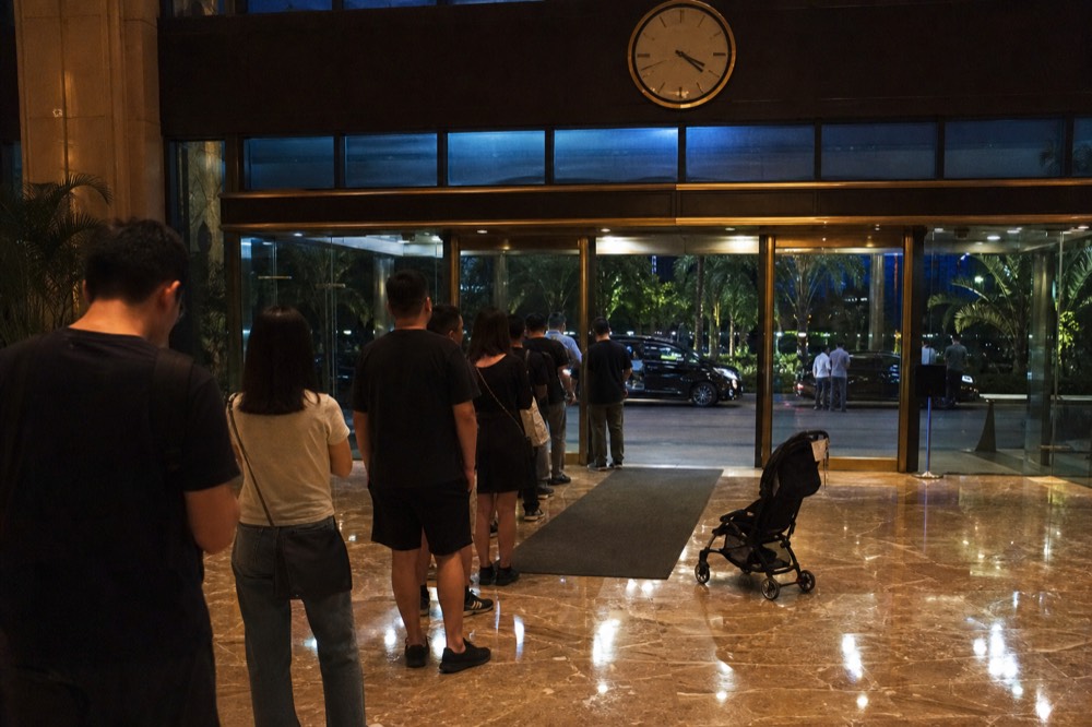Theatre lobby clock and entry doors with a small queue of guests arriving before a performance